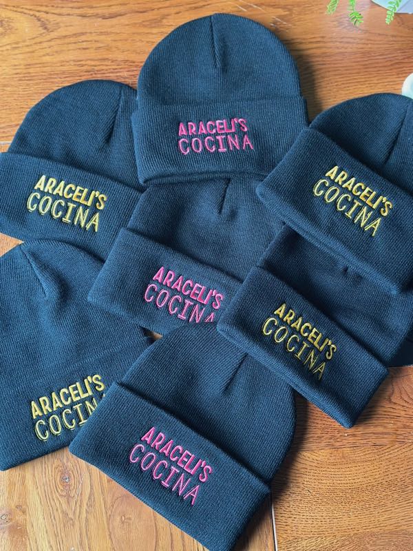 Black beanies embroidered with Araceli's Cocina in pink and yellow thread