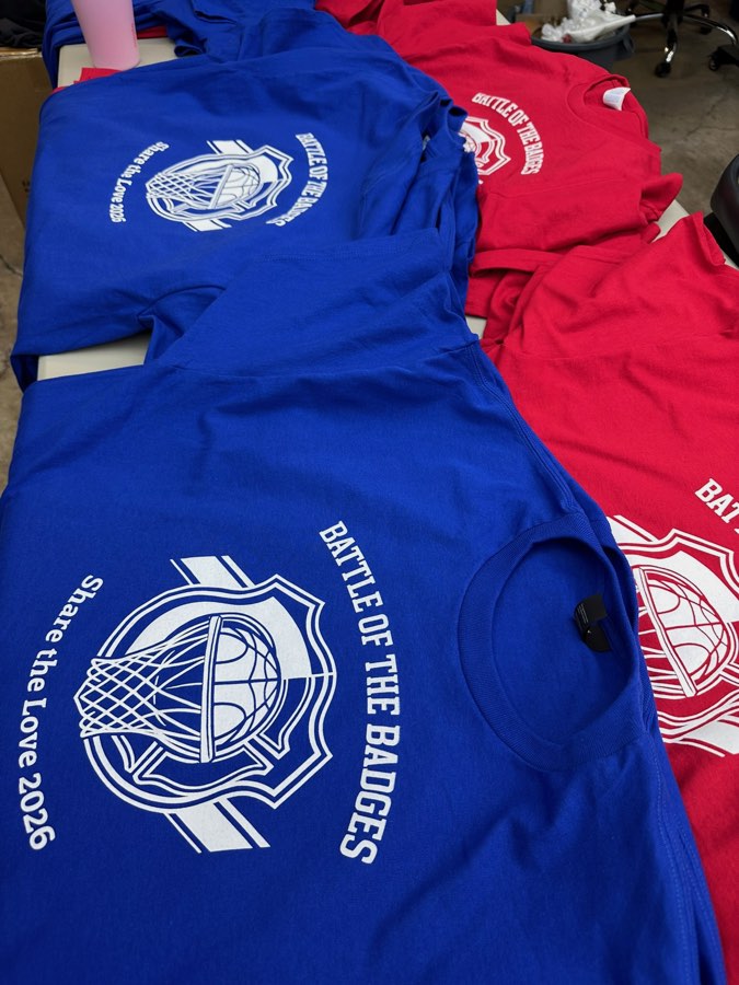 Blue and red Battle of the Badges 2026 event t-shirts laid out on a table