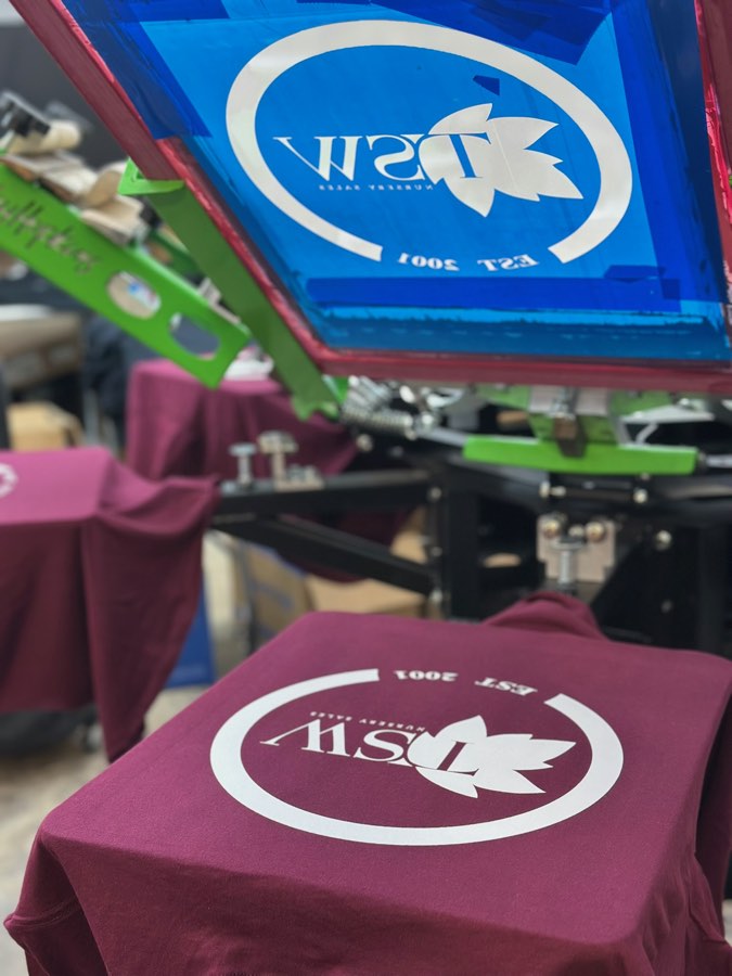 Maroon t-shirts being printed with a white logo on the Primal screen printing press