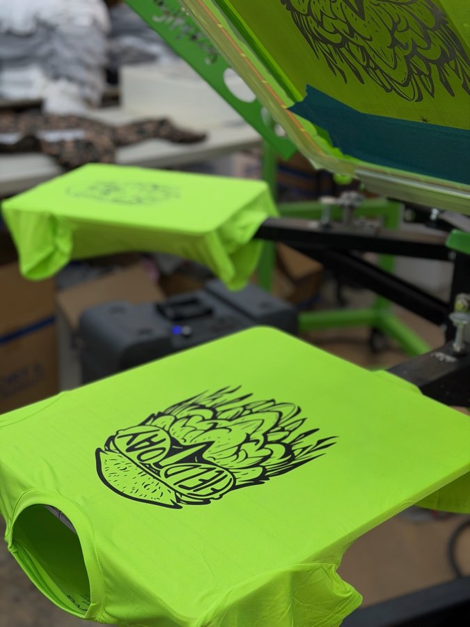 Neon green t-shirts being printed in black on the screen printing press