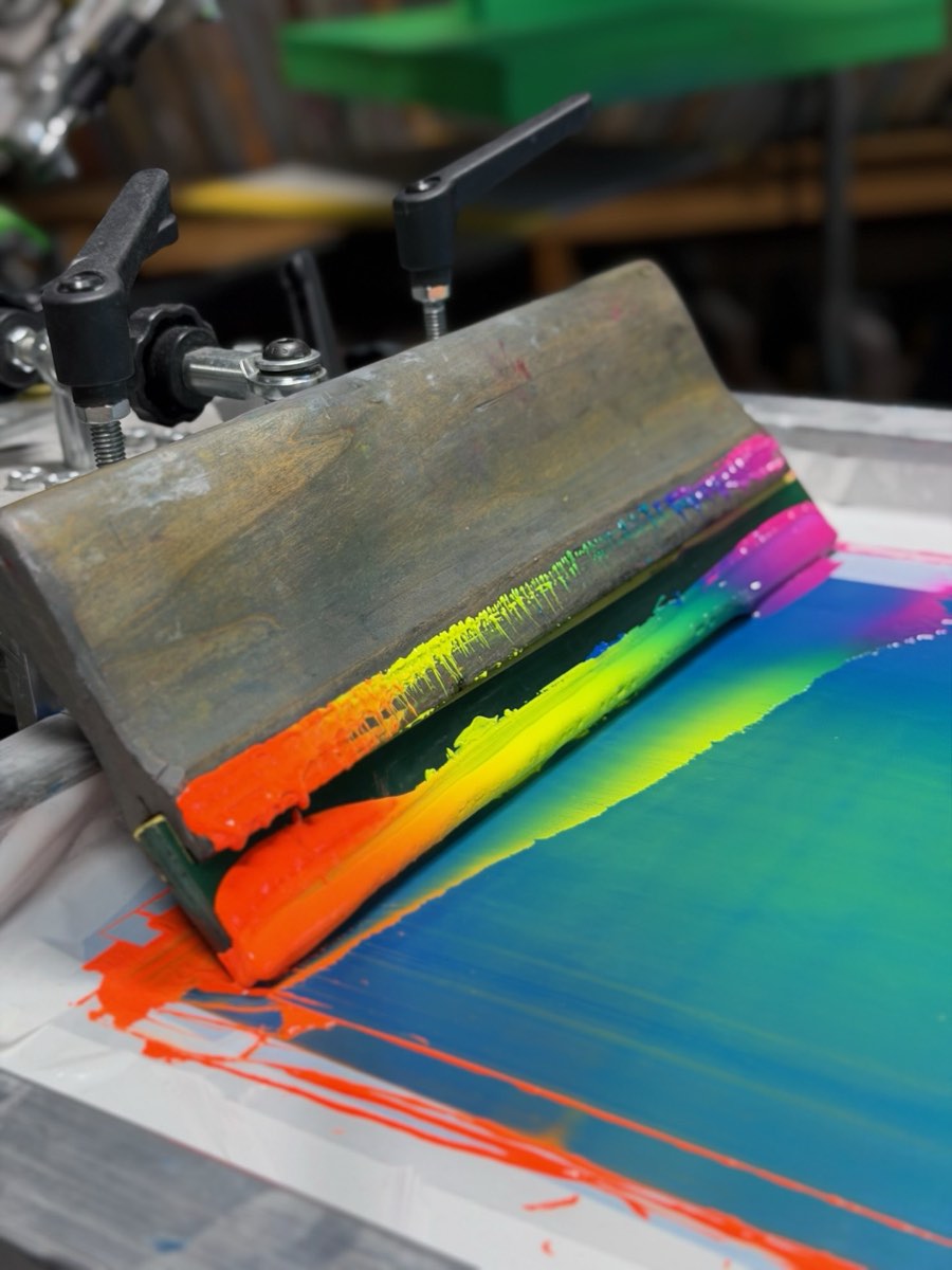 Squeegee pulling bright ink through a screen on the press at Primal Screen Printing