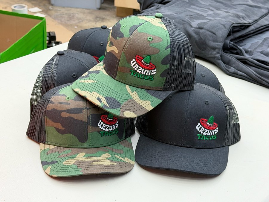 Camo and charcoal trucker hats with an embroidered red chili Urzua's logo